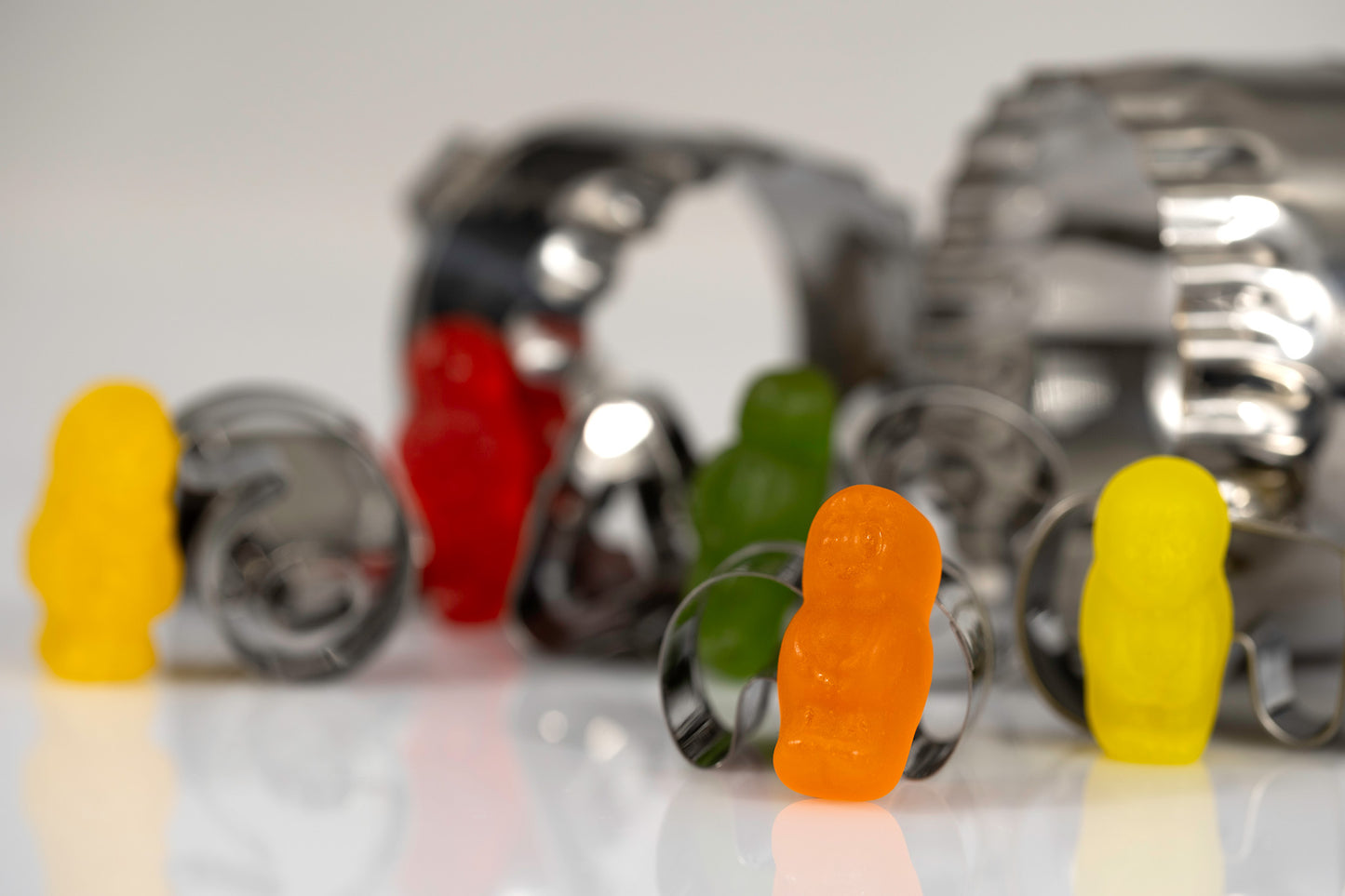 Orange, yellow, green and red miniature figures standing independently among scattered metal baking cutters.