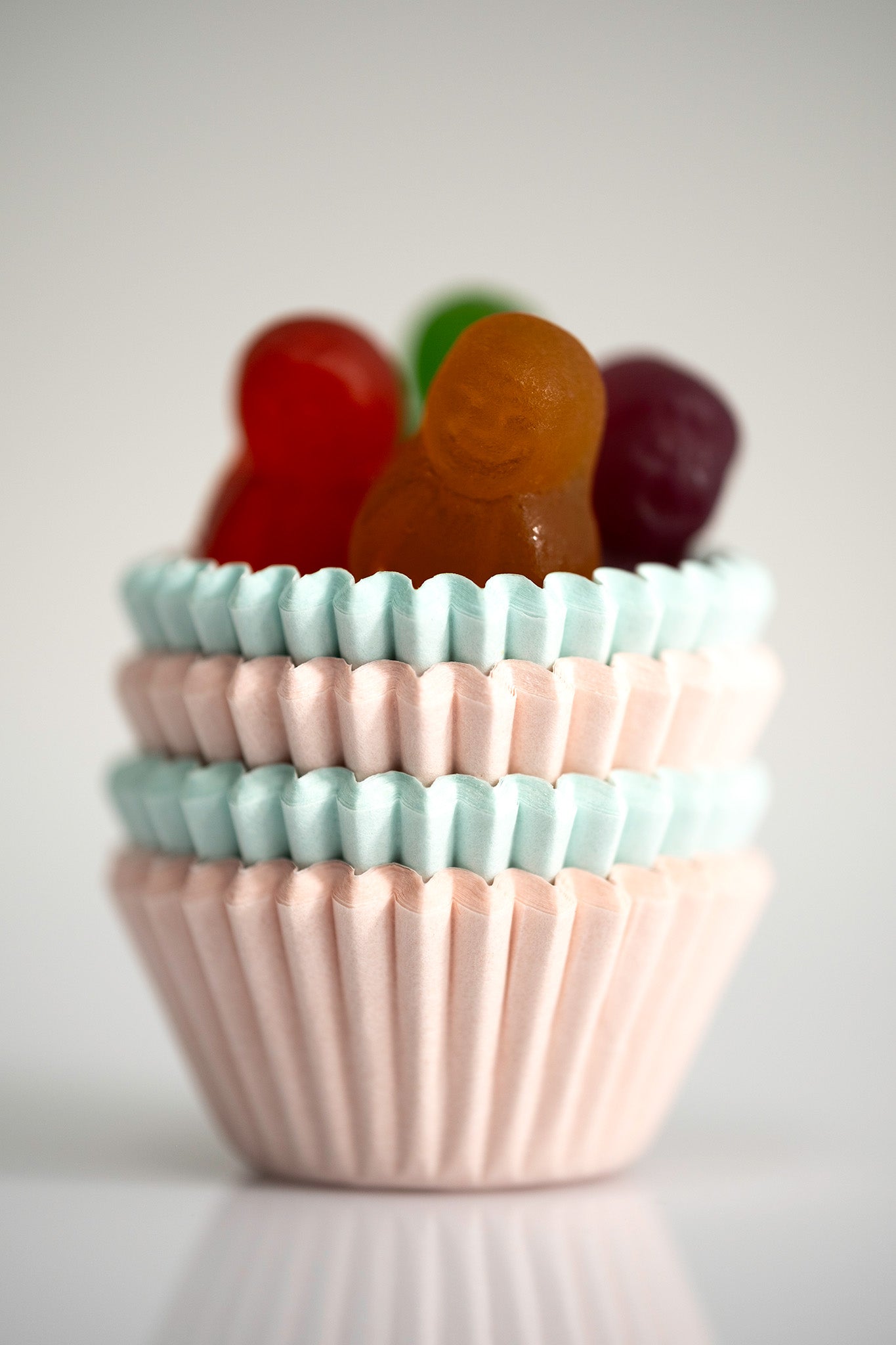 Orange, red, green and purple miniature figures emerging from alternating layers of pink and blue cupcake cases.