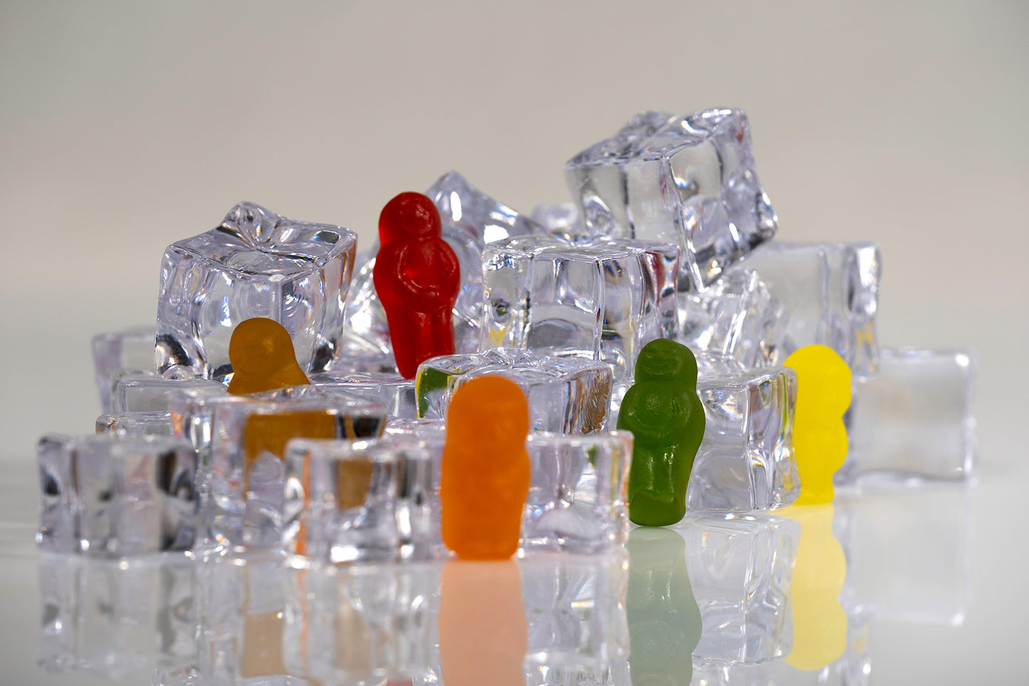 Colourful gummy figures positioned at different levels within a miniature landscape constructed from clear ice cubes.