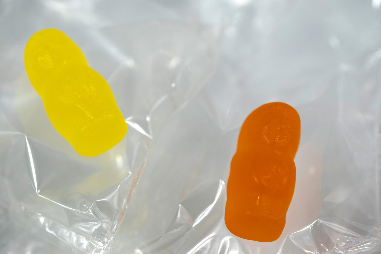 Two translucent yellow and orange baby-shaped figures floating against crumpled transparent material.