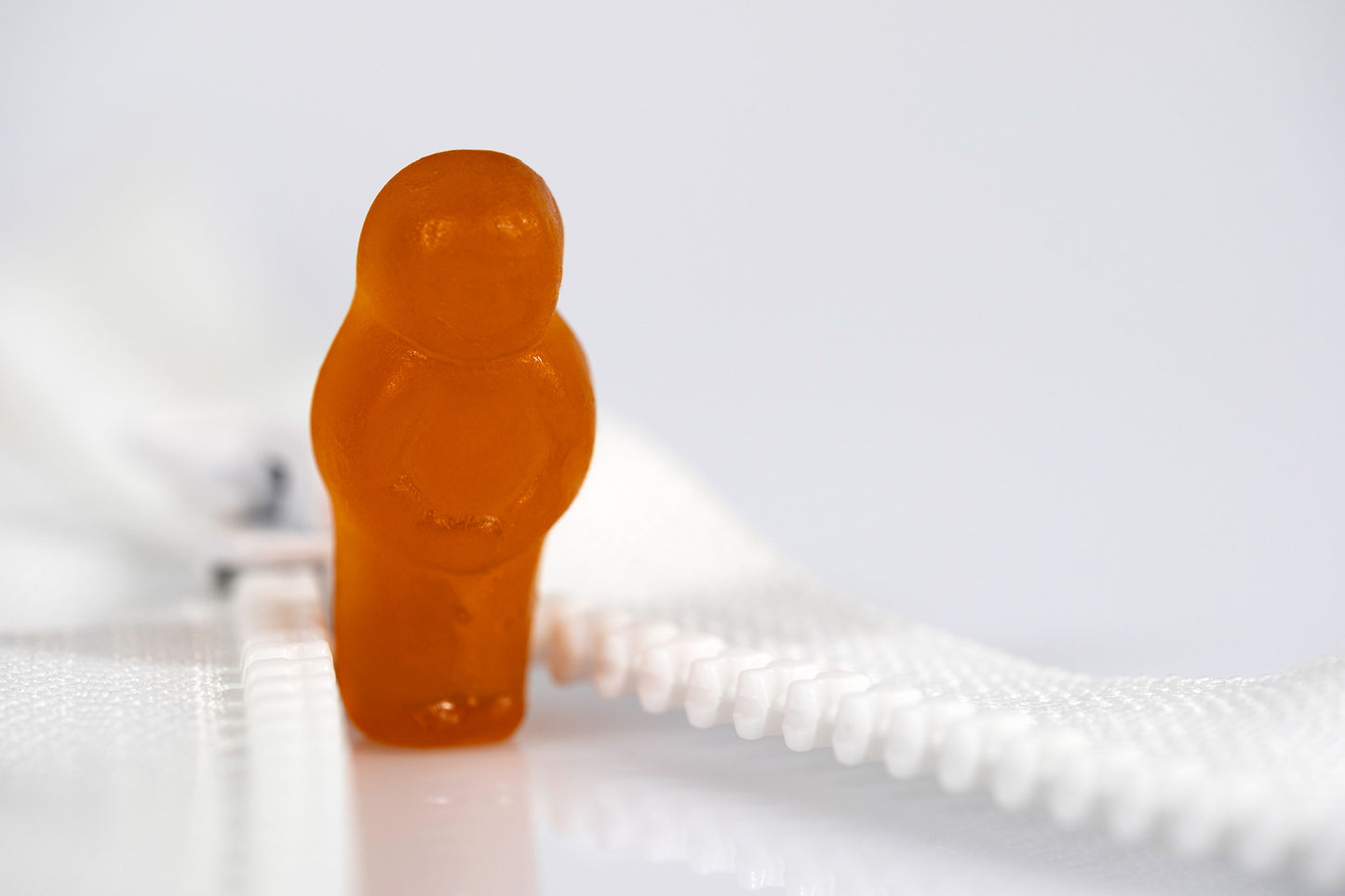 Orange confectionery figure standing between the receding sides of an open white zip against a soft white background.
