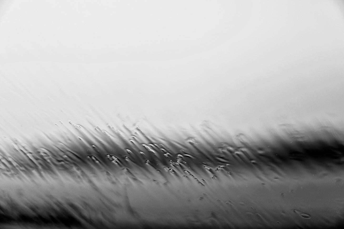 Coastal Noir 7669 - 90x60cm, monochrome photograph of rippling water and shoreline blurred by rain droplets on glass, minimalist abstract coastal print.