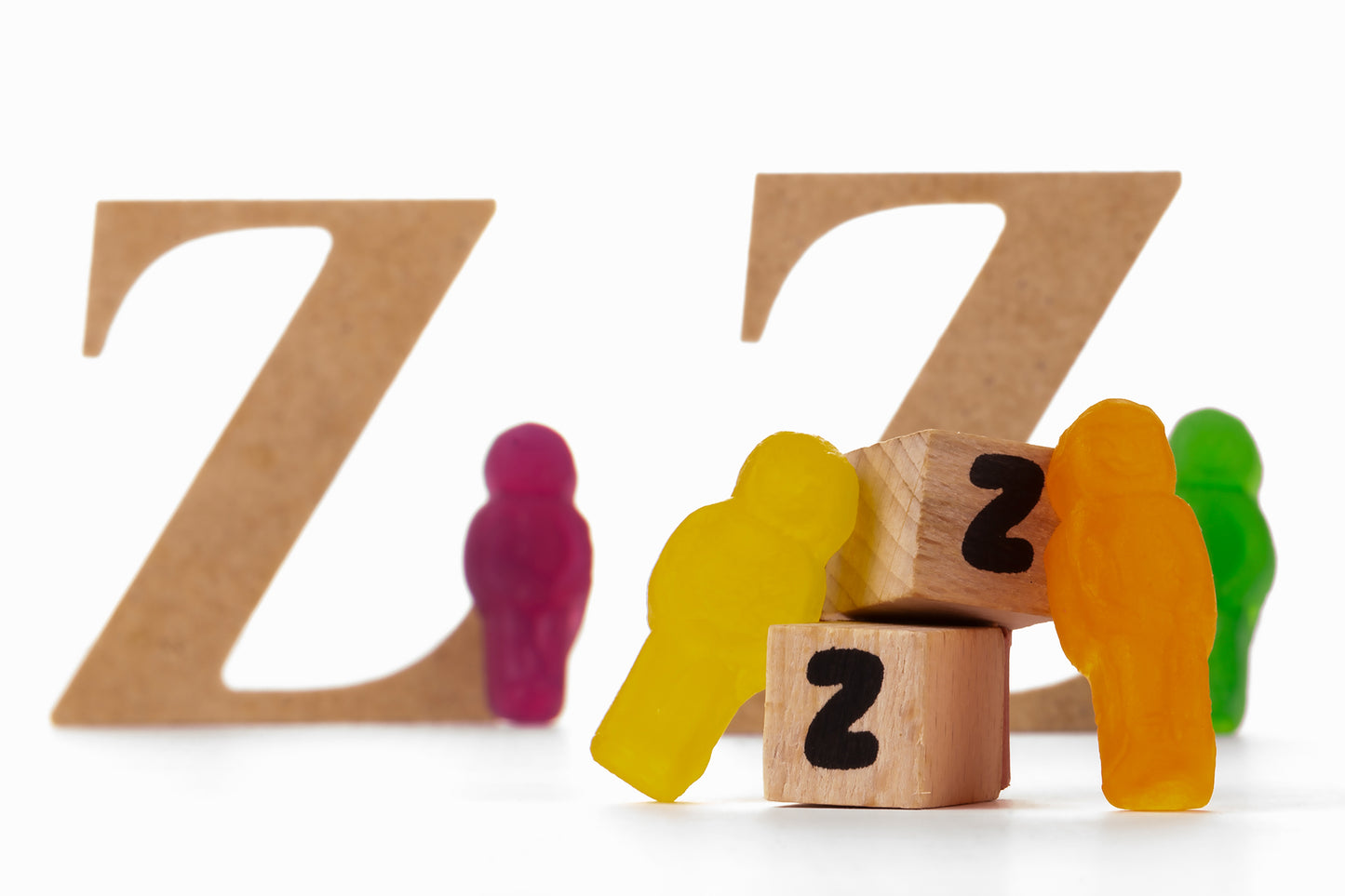 Catching Some ZZZ's 1493v3 - 90x60cm, playful fine art photograph featuring multicoloured jelly figures resting against wooden blocks marked with the letter Z, backed by large cardboard Zs, limited edition by Raymond Mather, ART1.