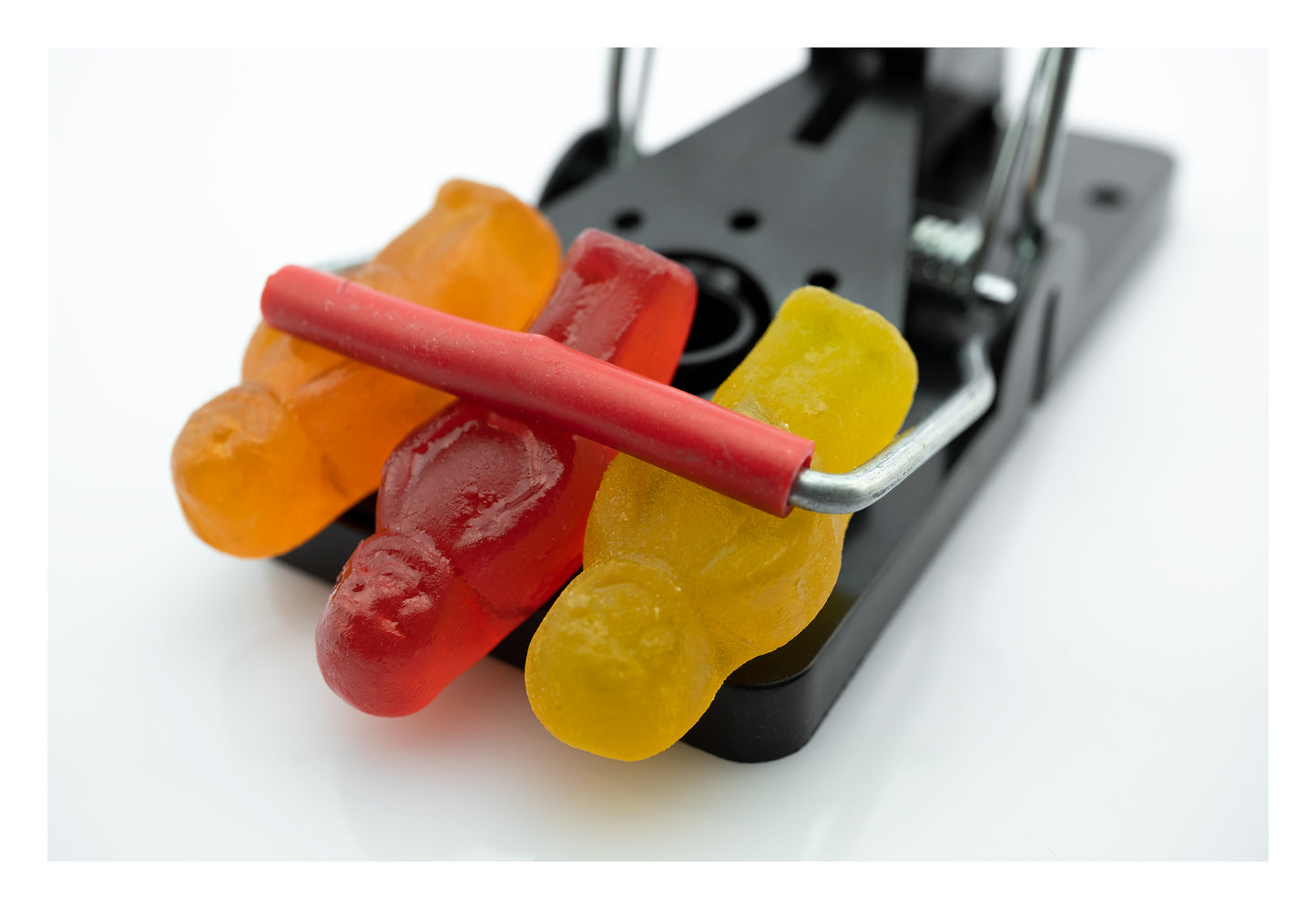 Caught in a Trap 3027 - 104x74cm, fine art photograph of three gummy jelly figures caught beneath the bar of a black metal trap, captured with precision and pop-art wit by Raymond Mather, ART1.