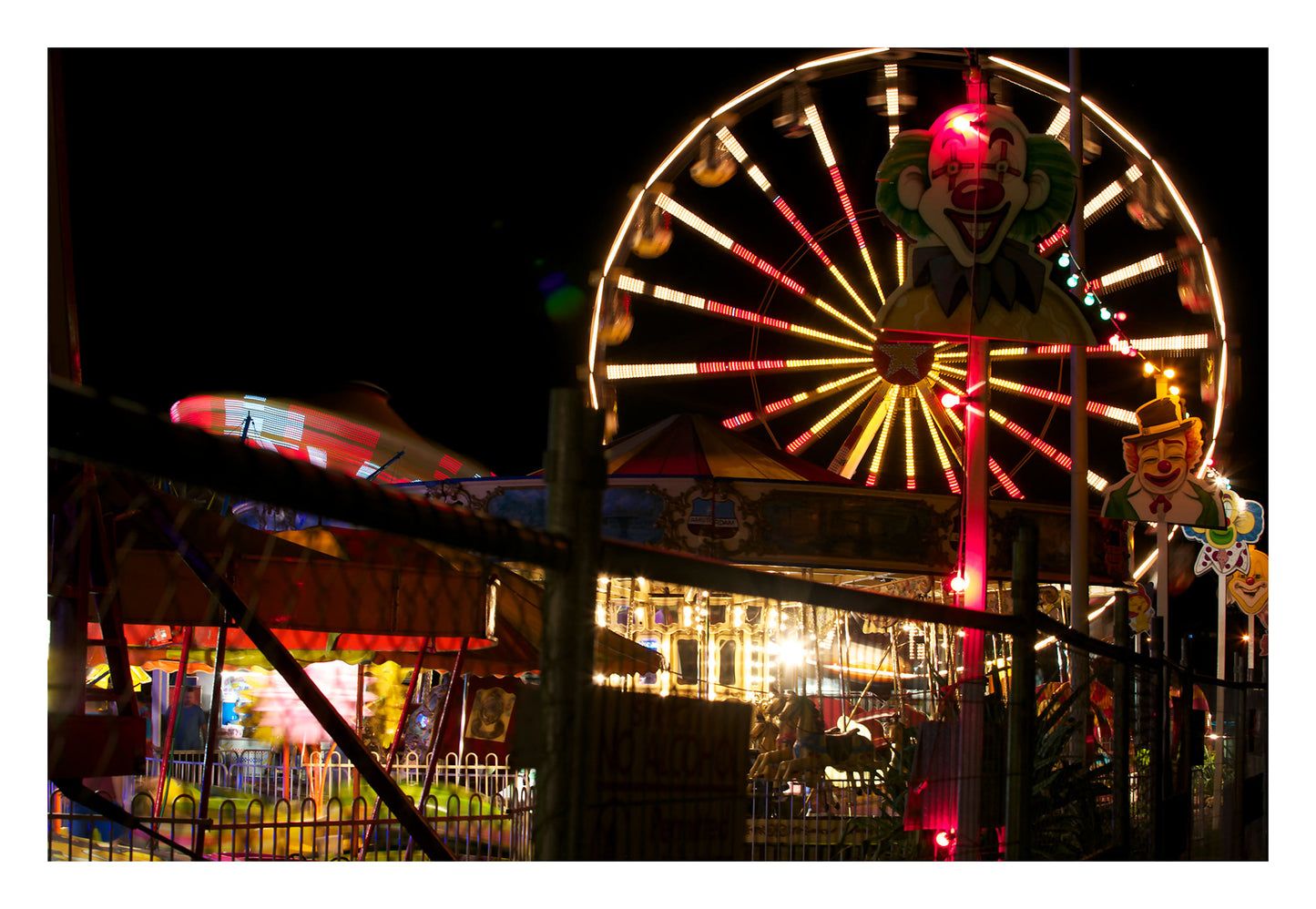 Fairground Carnival Lights 6900083 - 104x74cm, night carnival view with Ferris wheel, glowing rides, and striking clown figure, fine art limited edition print by Raymond Mather, ART1.