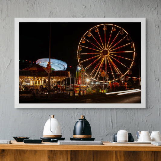 Fairground Carnival Lights 6900108 - Room View, a long exposure nighttime image capturing a glowing Ferris wheel, a spinning carousel in streaks of blue light, and vibrant fairground décor including clown signs and string lights. The photograph by Raymond Mather captures the immersive energy and joy of carnival nights.
