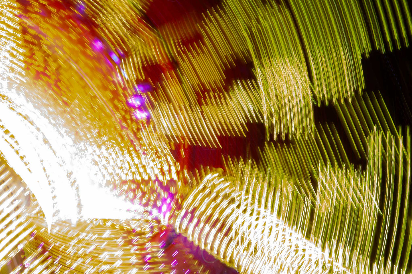 Fairground Carnival Lights 6900131 - 90x60cm, an abstract long exposure of carnival lights in motion, forming sweeping ribbons of gold, red, white, and purple across the frame. Captured by Raymond Mather, this fine art photograph transforms fairground energy into a dynamic light composition.