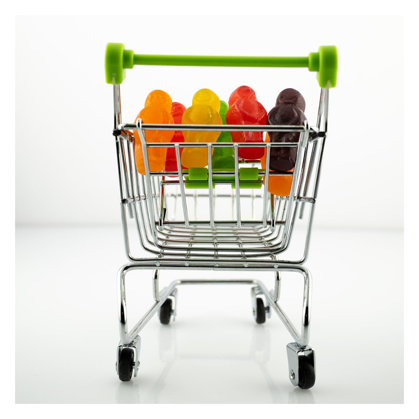 Gone Shopping 2303v1 - 104x104cm, colourful jelly baby figures packed neatly inside a miniature chrome shopping trolley with green handles, staged on a clean white background, fine art photography by Raymond Mather, ART1.