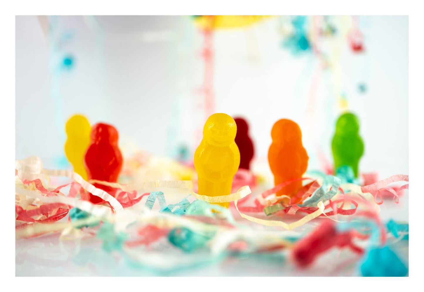 Life’s a Party 2417v2 - 104x74cm, colourful jelly baby figures surrounded by festive paper streamers on a reflective white surface, fine art photograph by Raymond Mather, ART1.