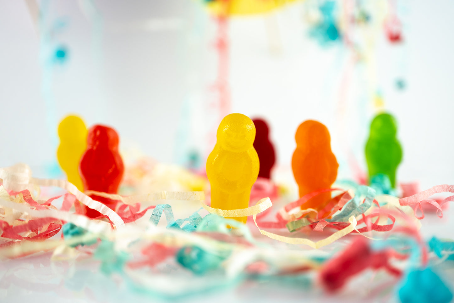 Life’s a Party 2417v2 - 90x60cm, colourful jelly baby figures surrounded by festive paper streamers on a reflective white surface, fine art photograph by Raymond Mather, ART1.