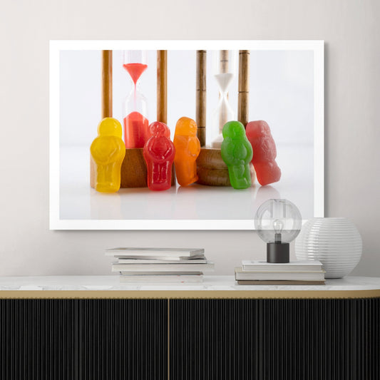 Like Sands Through the Hourglass 2678v1 - Room View, whimsical still life of colourful jelly baby figures standing beside vintage sand timers with red and white sand, reflecting time, nostalgia, and childhood in a playful conceptual fine art photograph by Raymond Mather, ART1.