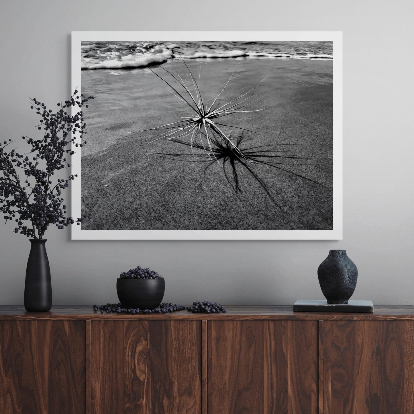 Monochrome Mix - Beach - Spinifex - 184017 - Room View, A black and white coastal image showing a spinifex plant with its dramatic shadow stretching across the sand, with gentle waves in the background. Limited edition fine art print.
