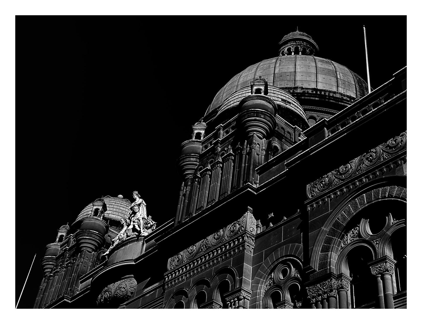 Monochrome Mix - Sydney - QVB - 231101v3 - 104x81.5cm, Black and white photograph of the Queen Victoria Building in Sydney, featuring ornate domes, detailed façade architecture, and classical sculpture against a dark sky.