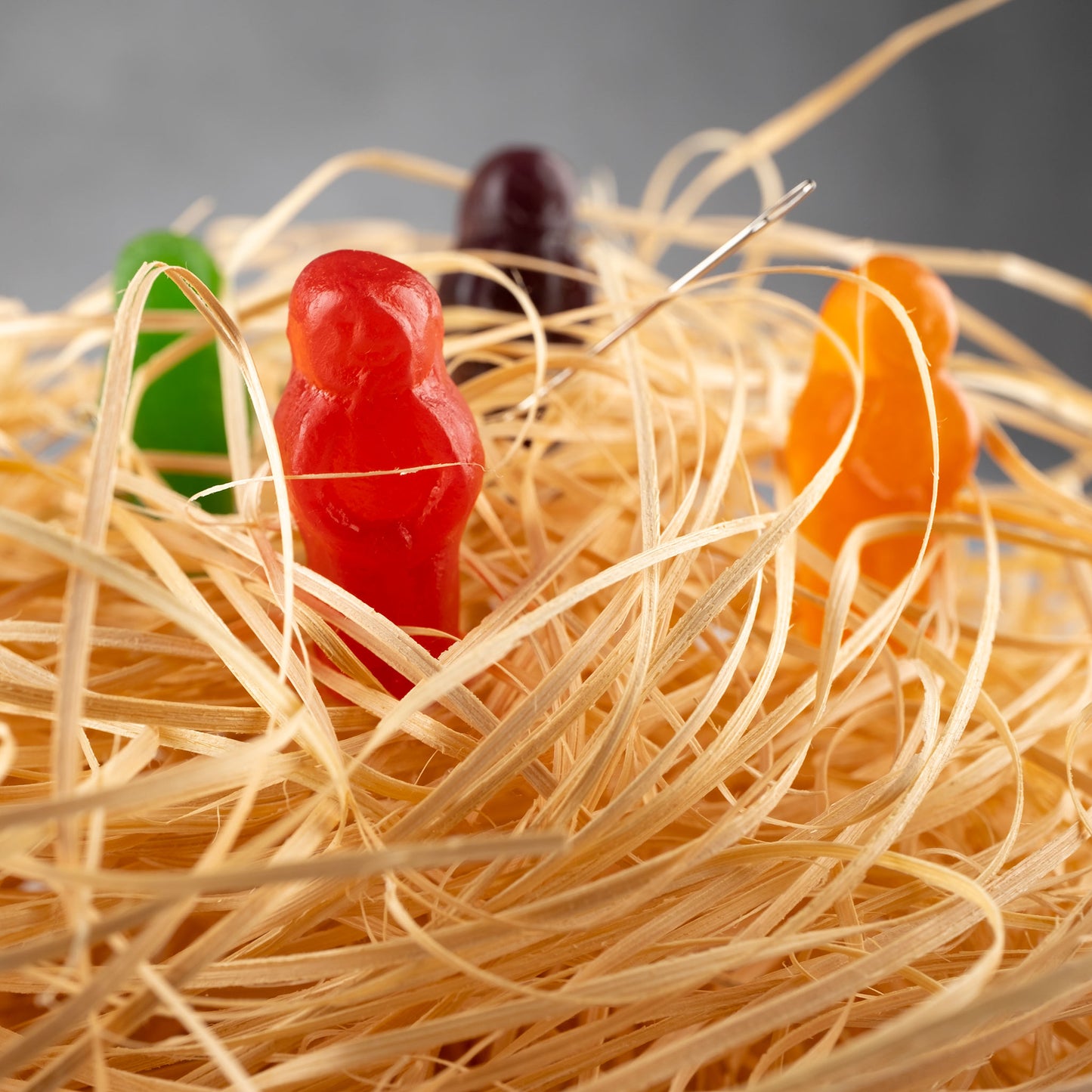 Needle in a Haystack 2523v1 - Close Detail View, conceptual fine art photograph by Raymond Mather featuring colourful jelly baby figures nestled in straw with a real sewing needle subtly placed, playfully reimagining the classic idiom in vibrant pop art style.