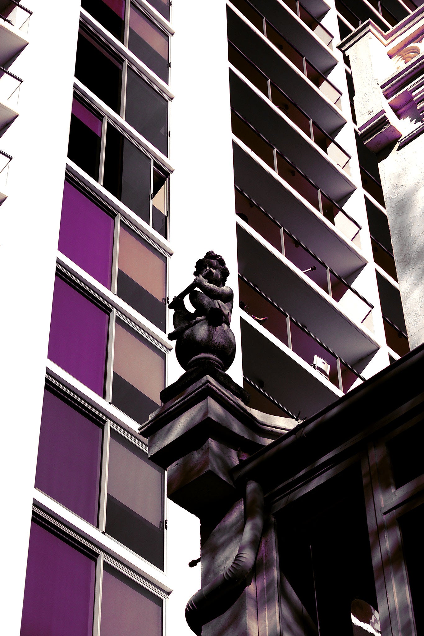POPscape Sydney - Darlinghurst - Building Statue - 1906064v16 - 60x90cm, Stylised image of a cherub statue atop a heritage building, surrounded by modern high-rise architecture in Darlinghurst. Muted purples and dark tones create dramatic Pop Art contrast.