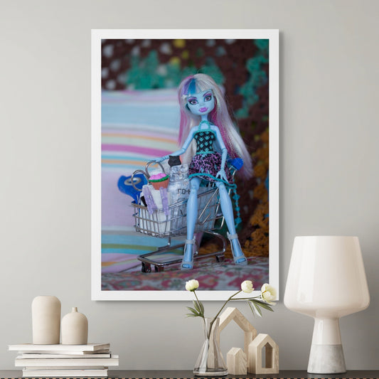 Trolley Dolly - Series No.1: 197147 - Room View, a blue skinned fashion doll with pastel hair sits inside a miniature shopping trolley filled with handmade props including a cupcake, bag, and clipped paper rolls. Set against a striped and crocheted background, the image explores themes of homelessness, childhood, and resilience.