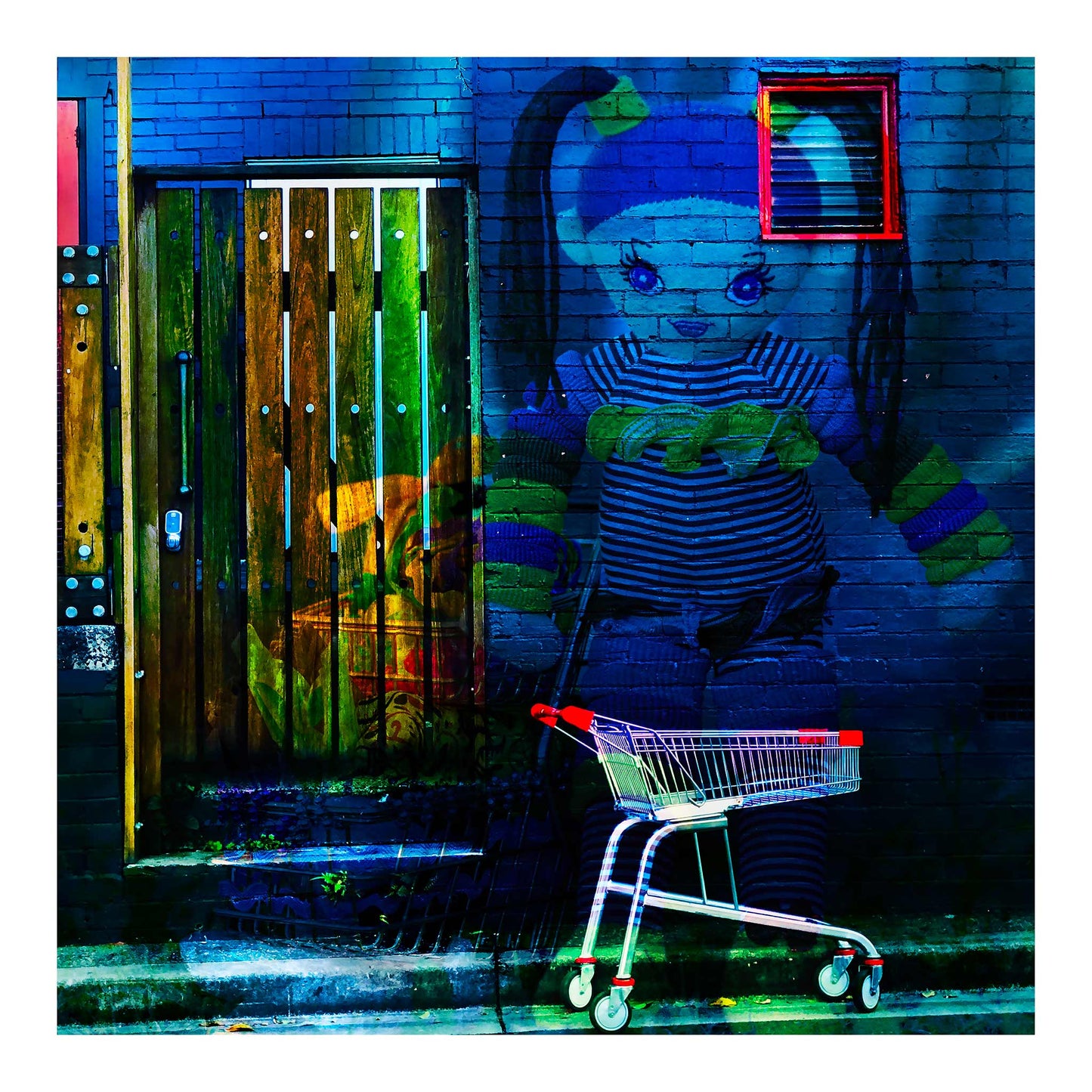 Trolley Dolly - Series No.2: 19E2255v14 - 74x74cm, a knitted doll with striped clothing and ponytails appears against a dark blue brick wall. A red-handled shopping trolley sits below, and a wooden door to the left glows with market textures and shadow. The surreal image explores homelessness and emotional vulnerability.