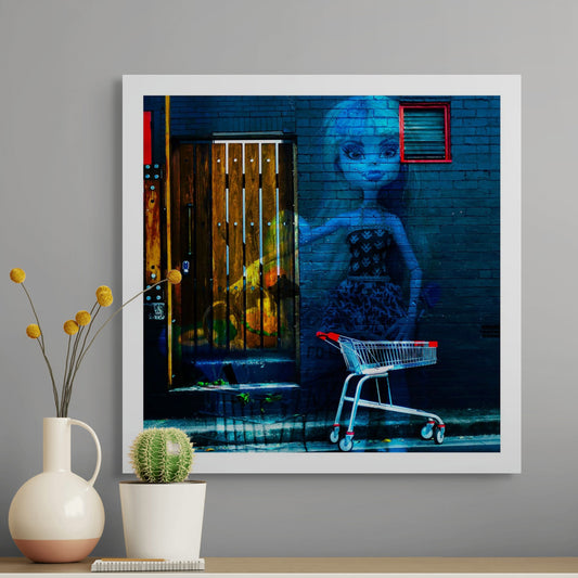 Trolley Dolly - Series No.2: 19E2255v4 - Room View, a translucent doll in a patterned dress is superimposed on a dark brick wall beside a red-handled shopping trolley. A wooden door, partially layered with ghostly fruit imagery, adds symbolic depth. The composition explores homelessness, invisibility, and femininity in an urban context.