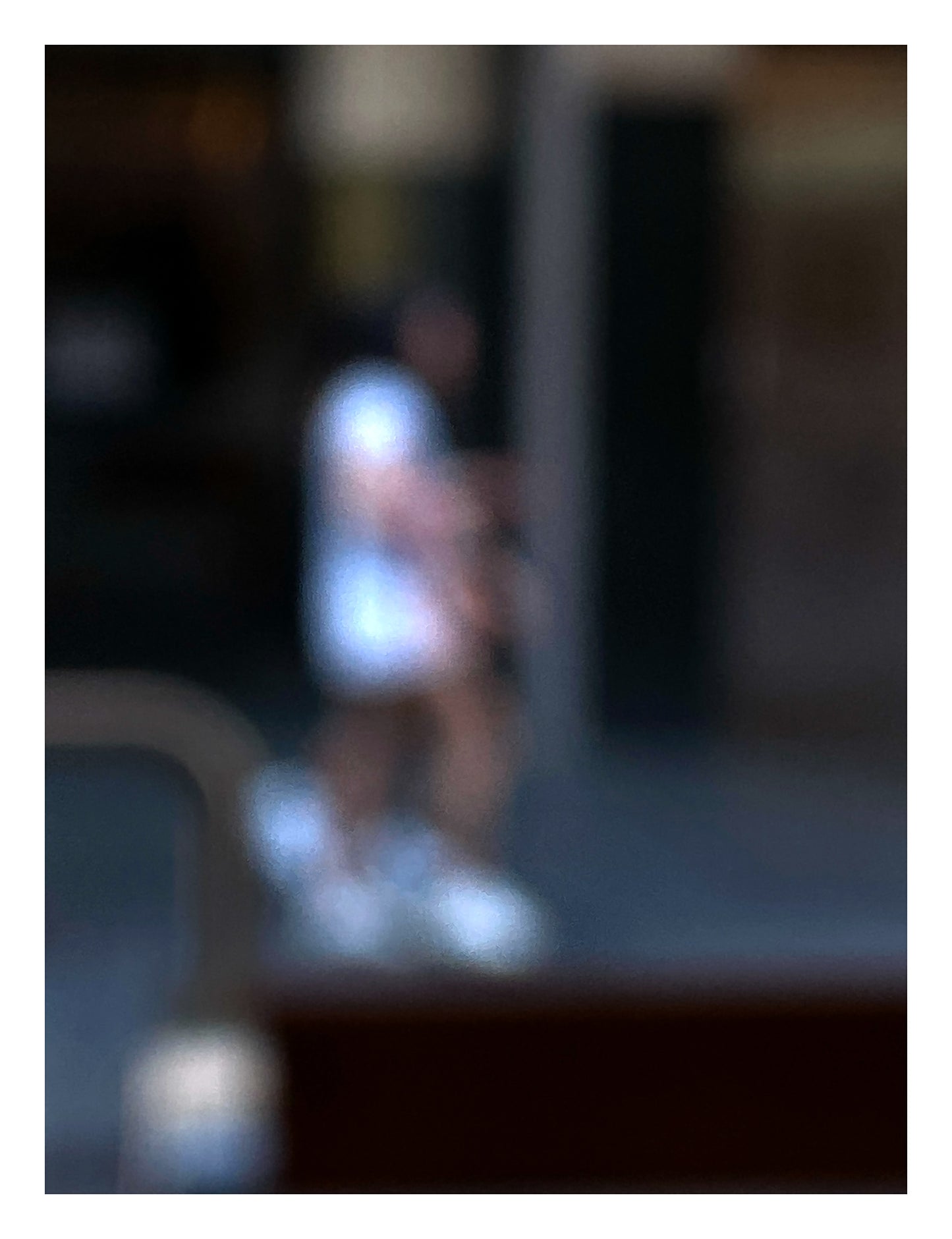 Urban Commute - Series No.1: 0979v1 - 81.5x104cm, a soft focus photograph of two city walkers side by side, dressed in light tones with glowing white shoes, set against a deep urban backdrop. A gesture of shared movement and quiet rhythm. Limited edition fine art print by Raymond Mather.