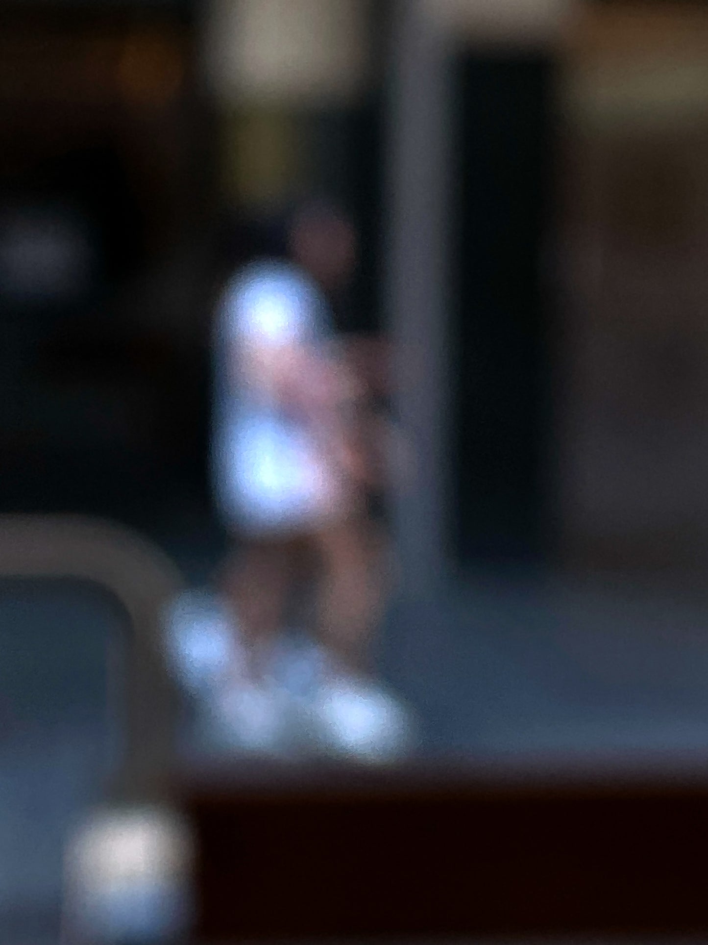 Urban Commute - Series No.1: 0979v1 - 67.5x90cm, a soft focus photograph of two city walkers side by side, dressed in light tones with glowing white shoes, set against a deep urban backdrop. A gesture of shared movement and quiet rhythm. Limited edition fine art print by Raymond Mather.
