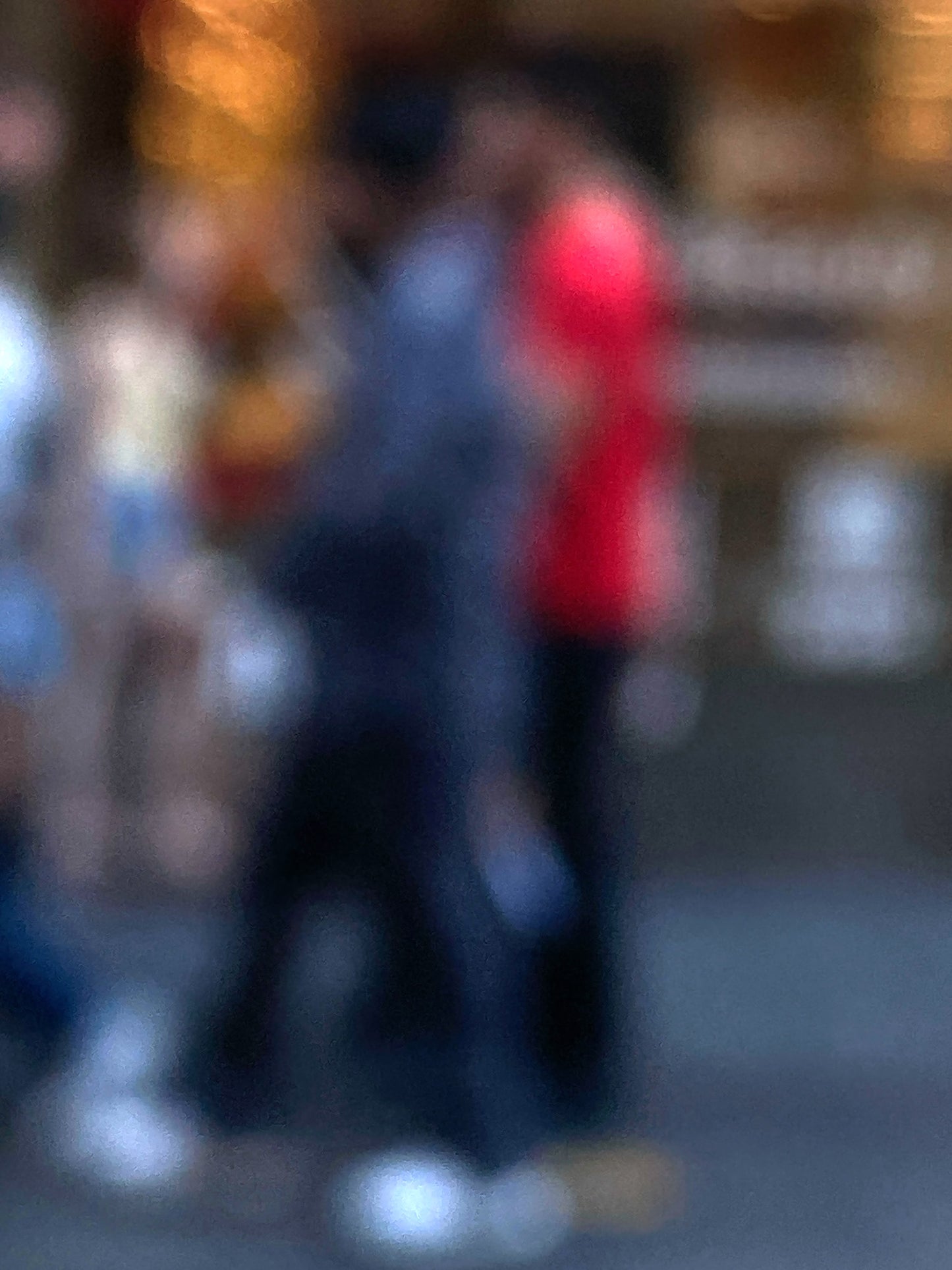 Urban Commute - Series No.1: 0983v1 - 67.5x90cm, a soft focus photograph of blurred pedestrians in motion, with one figure in bright red passing a golden-lit city storefront. A painterly exploration of rhythm, anonymity, and colour in the urban commute. Limited edition fine art print by Raymond Mather.
