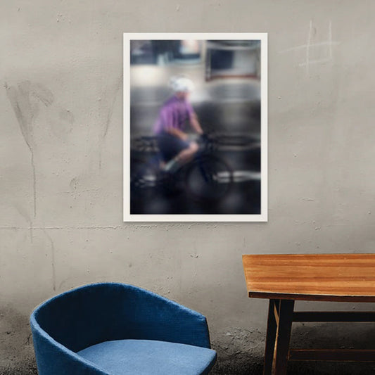 Urban Commute, Series No.2: 8621(1)v1 - Room View, fine art photograph by Raymond Mather featuring a blurred cyclist in purple shirt and white helmet, riding through a moody, reflective cityscape. The image is softly distorted, blending motion with atmosphere in a dreamlike urban abstraction.