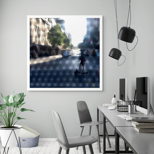 Urban Commute - Series No.2: 9230v1a - Room View, fine art photograph by Raymond Mather featuring a silhouetted scooter rider crossing a sunlit city street. Seen through a patterned screen, the image blends light, blur, and architectural rhythm into a poetic urban abstraction.