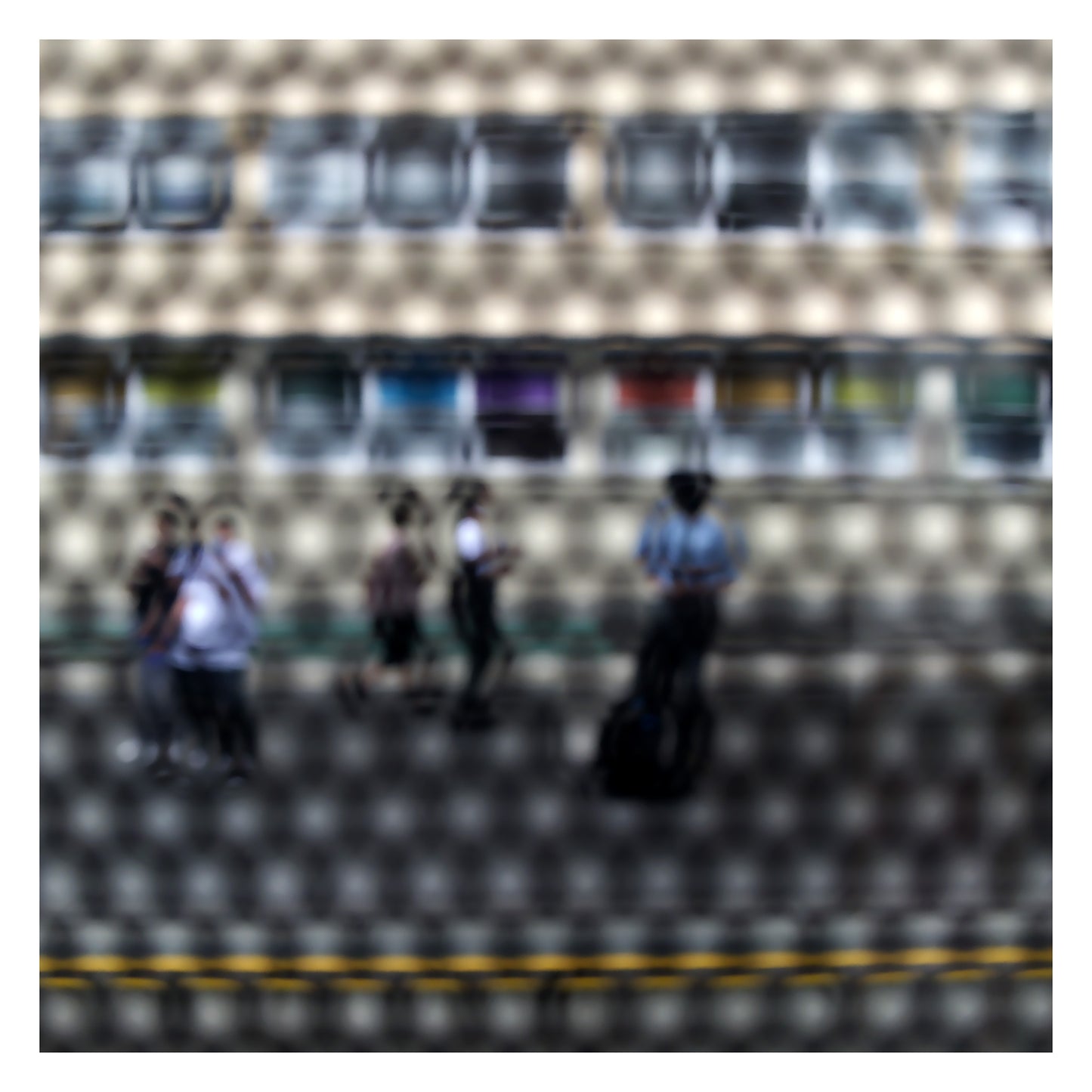 Urban Commute - Series No.2: 9557(1)v1a - 104x104cm, fine art photograph by Raymond Mather showing a group of pedestrians viewed through a circular patterned screen, with a colourful row of panels or bins behind them. The scene is abstracted into a rhythmic visual composition.