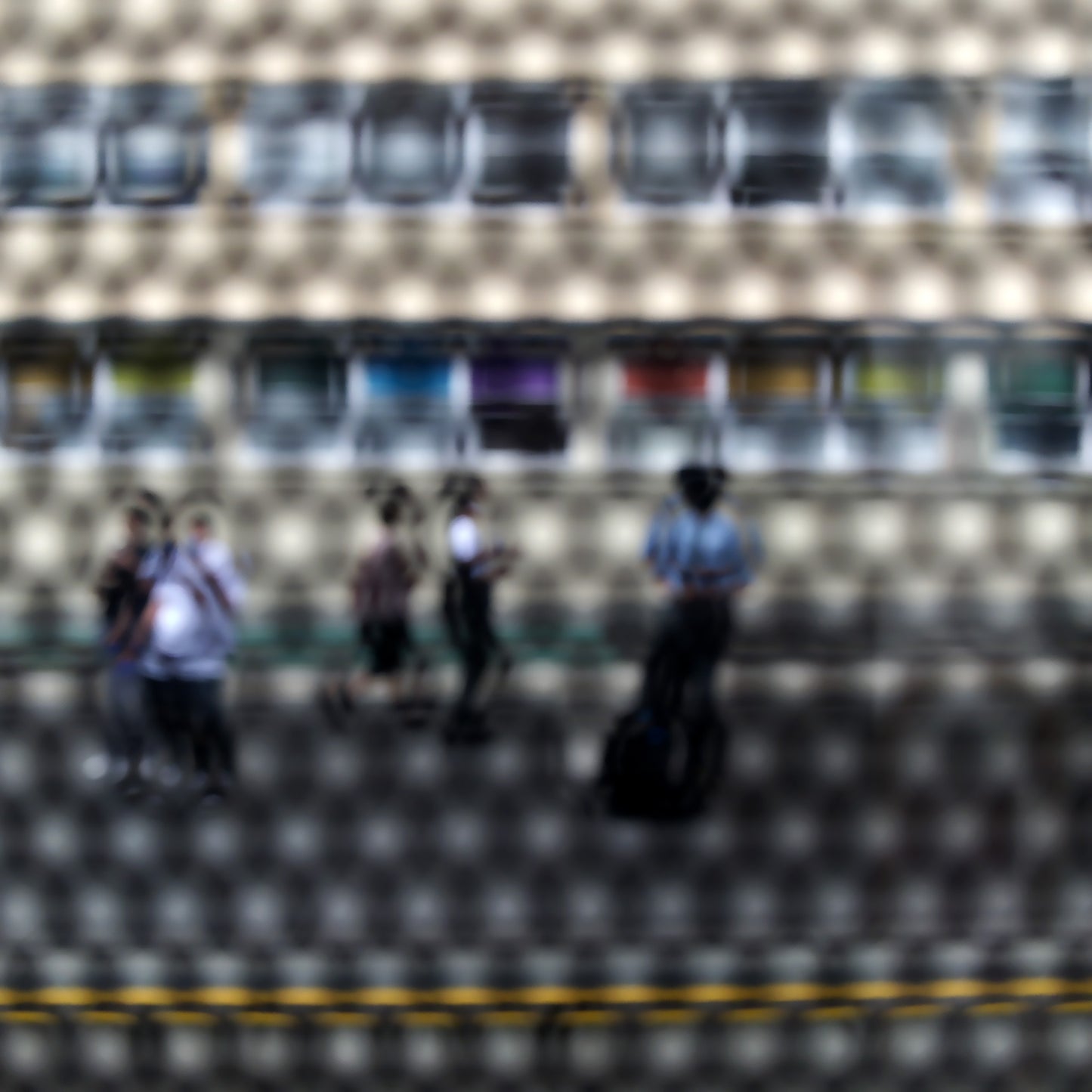 Urban Commute - Series No.2: 9557(1)v1a - 90x90cm, fine art photograph by Raymond Mather showing a group of pedestrians viewed through a circular patterned screen, with a colourful row of panels or bins behind them. The scene is abstracted into a rhythmic visual composition.