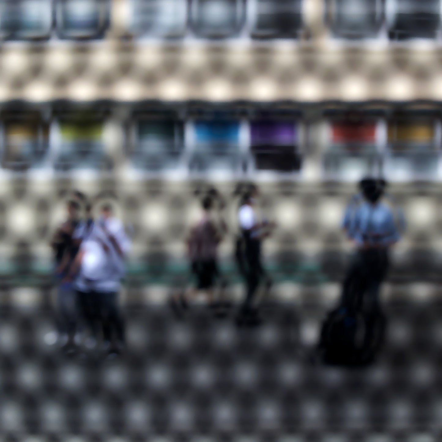 Urban Commute - Series No.2: 9557(1)v1a - Close Detail View, fine art photograph by Raymond Mather showing a group of pedestrians viewed through a circular patterned screen, with a colourful row of panels or bins behind them. The scene is abstracted into a rhythmic visual composition.