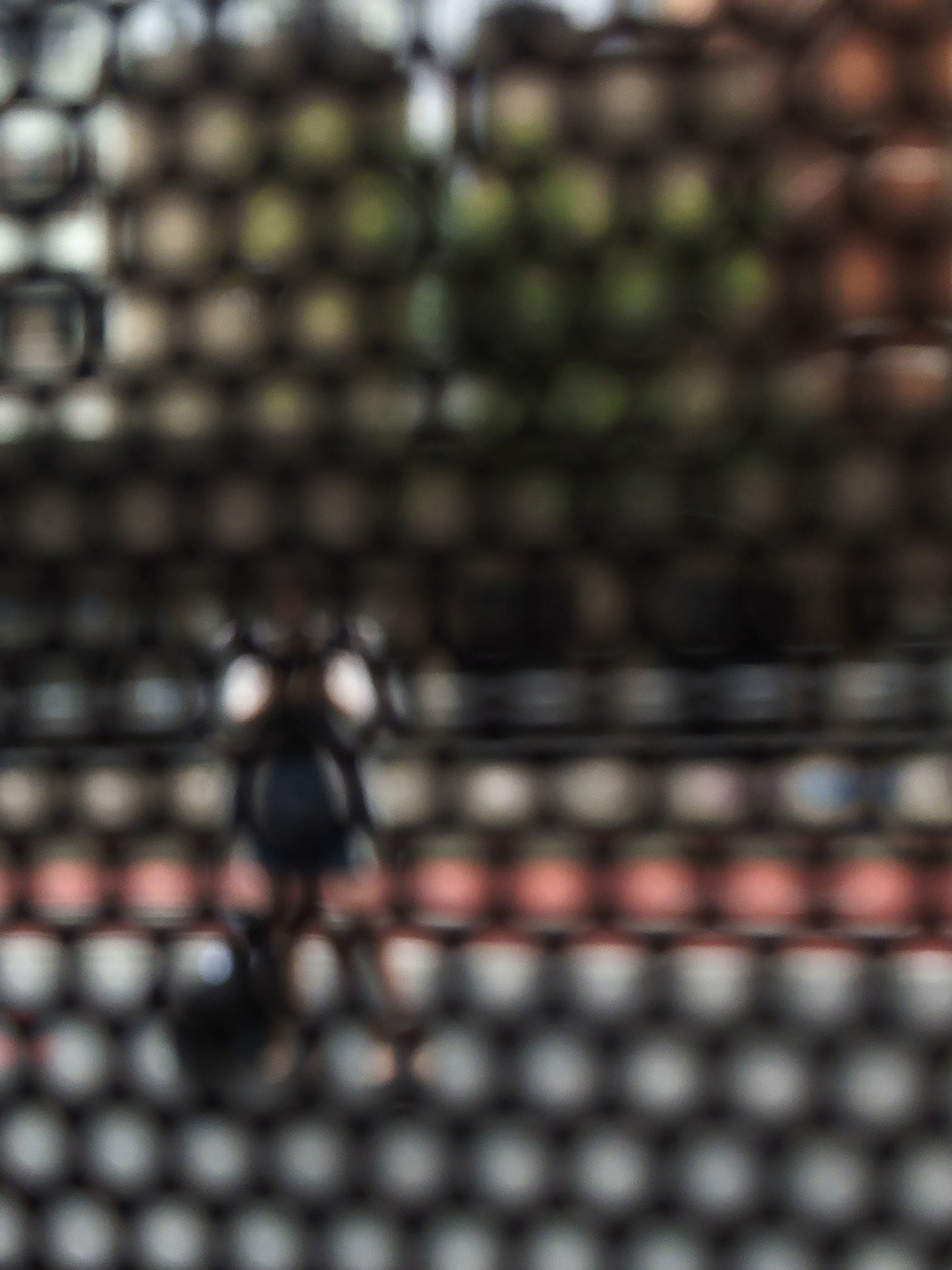 Urban Commute - Series No.2: 9568 - 67.5x90cm, fine art photograph by Raymond Mather featuring a blurred, solitary pedestrian viewed through a patterned screen. Muted tones and soft outlines evoke warmth, introspection, and urban stillness.