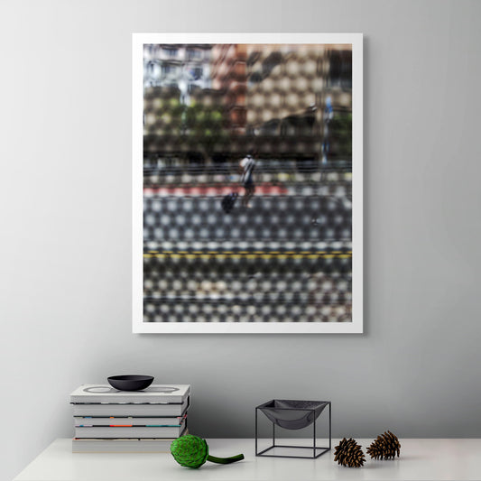 Urban Commute - Series No.2: 9569(1)v1 - Room View, fine art photograph by Raymond Mather featuring a lone blurred figure walking along a city street. Viewed through a dotted screen, the image blends red kerb, yellow line, and soft building reflections into a textured urban abstraction.