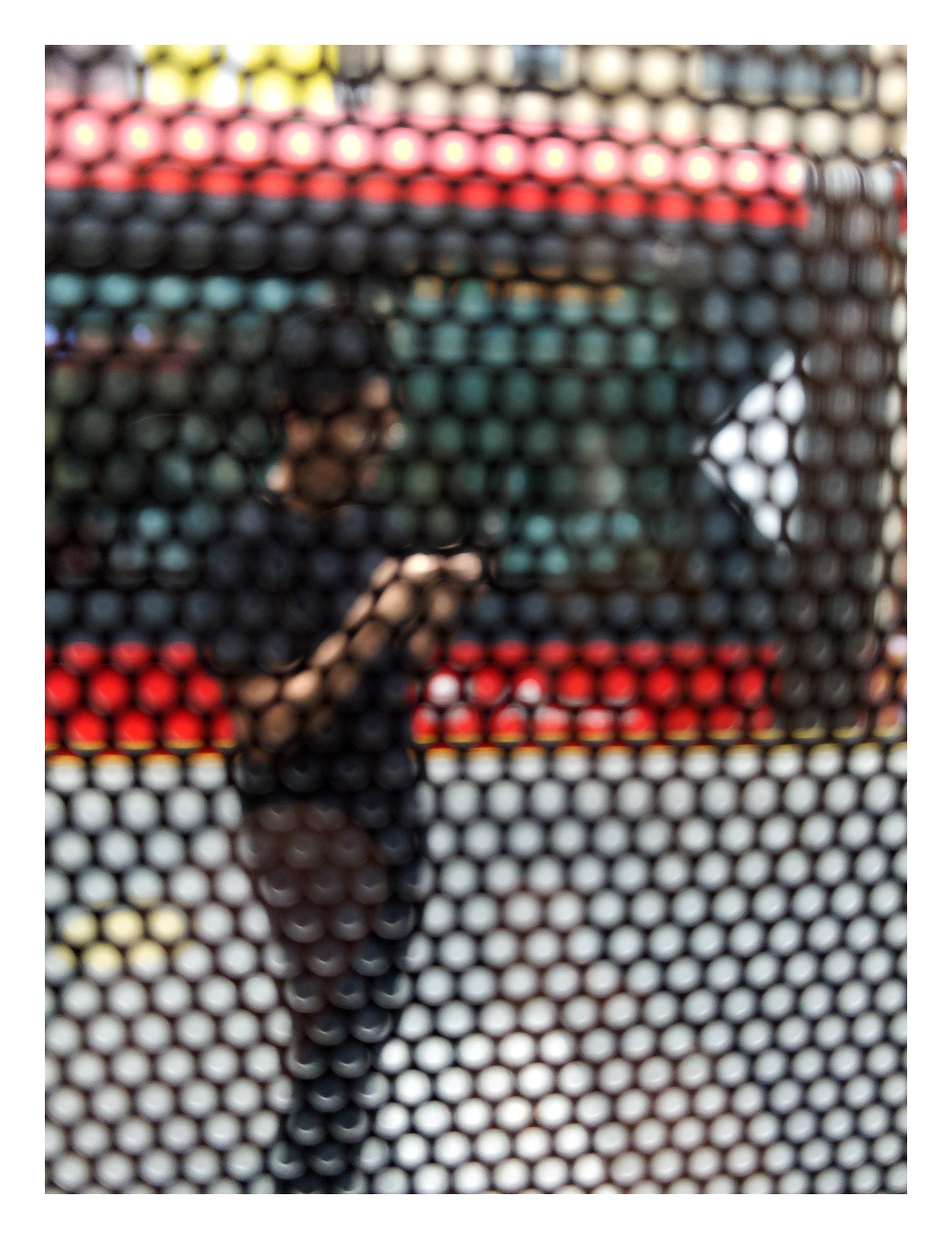 Urban Commute - Series No.2: 9574(1)v1 - 81.5x104cm, fine art photograph by Raymond Mather featuring a blurred figure using a phone, seen through a patterned screen with a red and green bus in the background. A richly layered urban image exploring distraction, movement, and modern life.