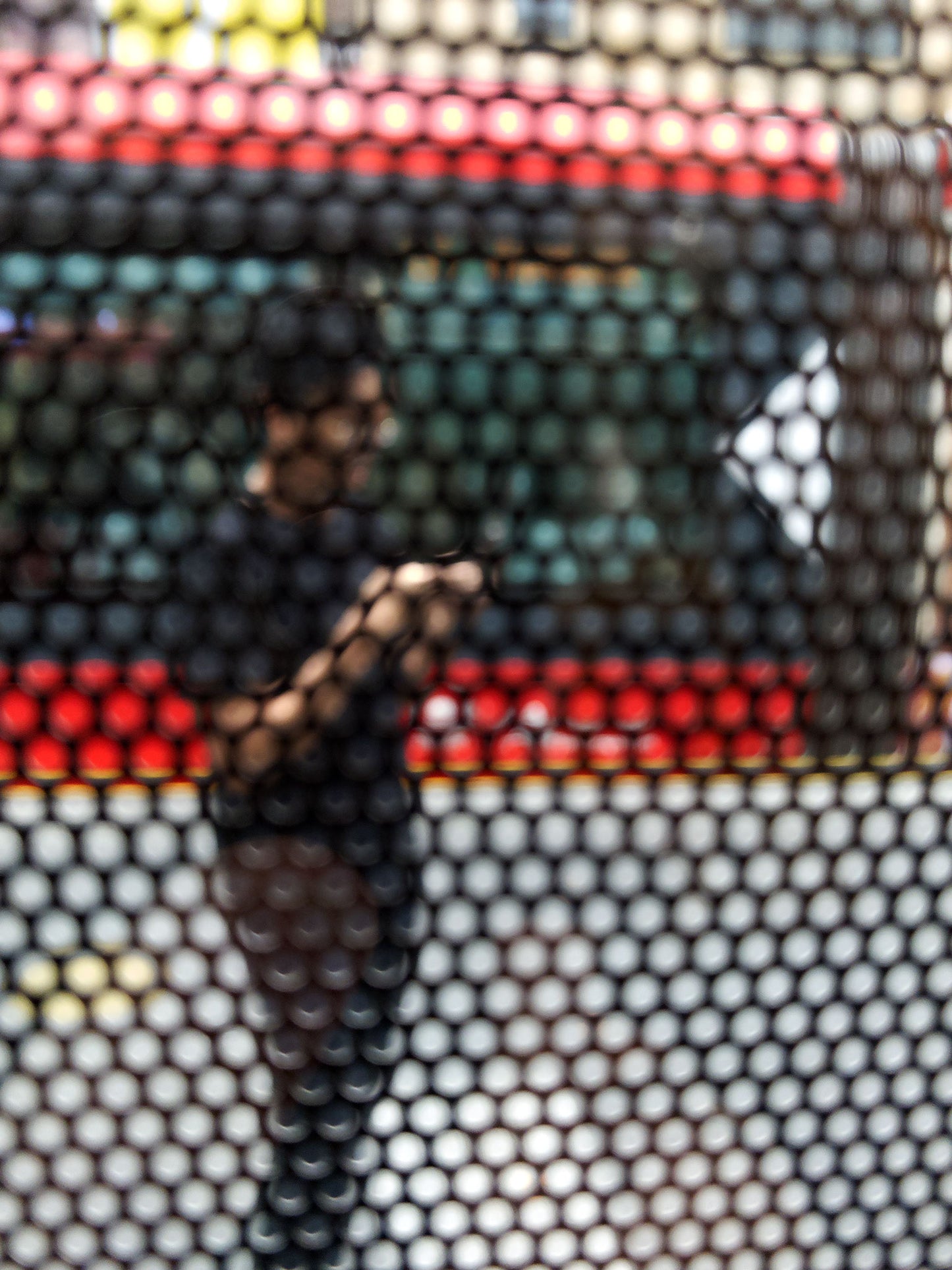 Urban Commute - Series No.2: 9574(1)v1 - 67.5x90cm, fine art photograph by Raymond Mather featuring a blurred figure using a phone, seen through a patterned screen with a red and green bus in the background. A richly layered urban image exploring distraction, movement, and modern life.
