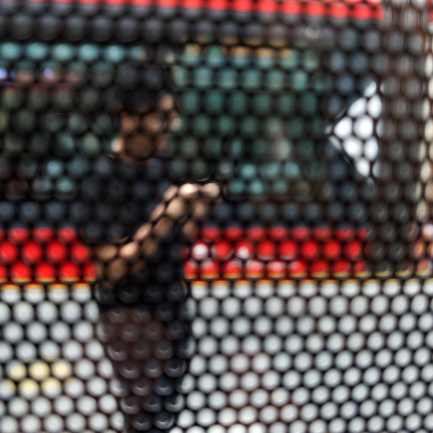 Urban Commute - Series No.2: 9574(1)v1 - Close Detail View, fine art photograph by Raymond Mather featuring a blurred figure using a phone, seen through a patterned screen with a red and green bus in the background. A richly layered urban image exploring distraction, movement, and modern life.