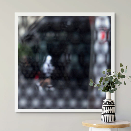 Urban Commute - Series No.2: 9590v1 - Room View, fine art photograph by Raymond Mather showing a blurred white-hooded figure walking across a dark city street, seen through a patterned screen. A haunting study in motion, texture, and introspection.