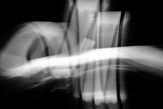 Black and white abstract long-exposure photograph created with light-drawing motion. Soft flowing shapes and sweeping white streaks move across a dark background, inspired by dance.