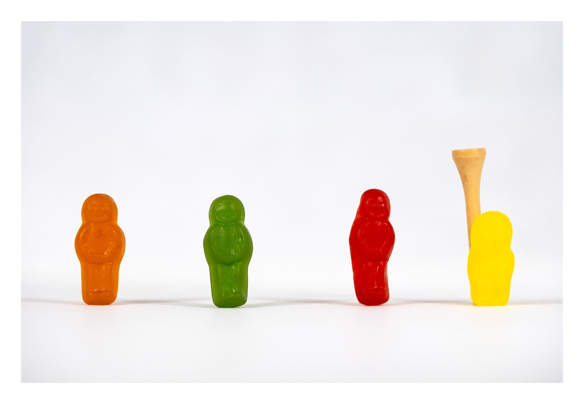 Four colourful confectionery figures in orange, green, red and yellow stand in a line beside a wooden golf tee in Teeing Off - 267089v1.