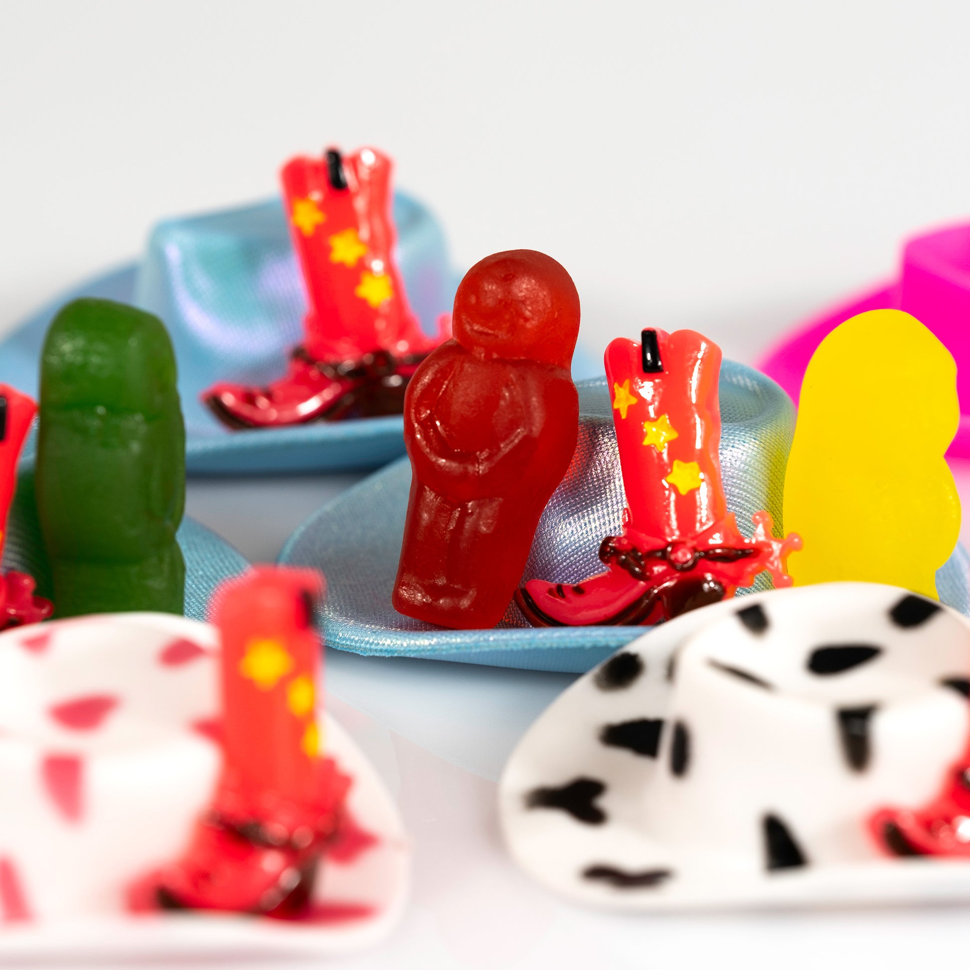 Close view of Boot Scootin Baby showing red and green jelly babies surrounded by miniature cowboy hats and bright red boots, ART1.