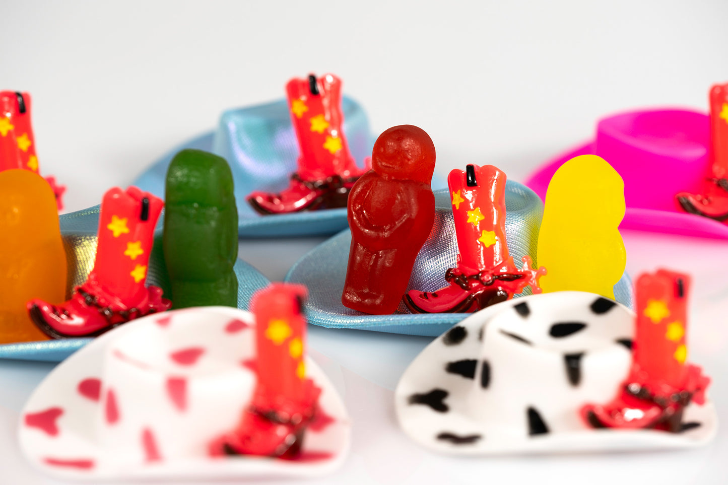 Boot Scootin Baby by Australian photographer Raymond Mather, colourful jelly babies gathered among miniature cowboy hats and red cowboy boots, ART1.