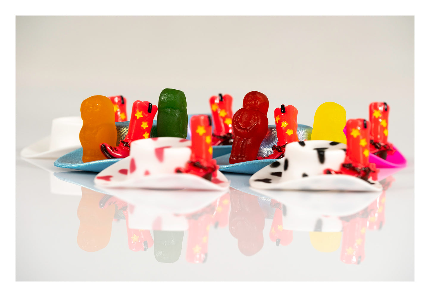 Colourful gummy figures and miniature red cowboy boots arranged on blue hats in a contemporary still life.