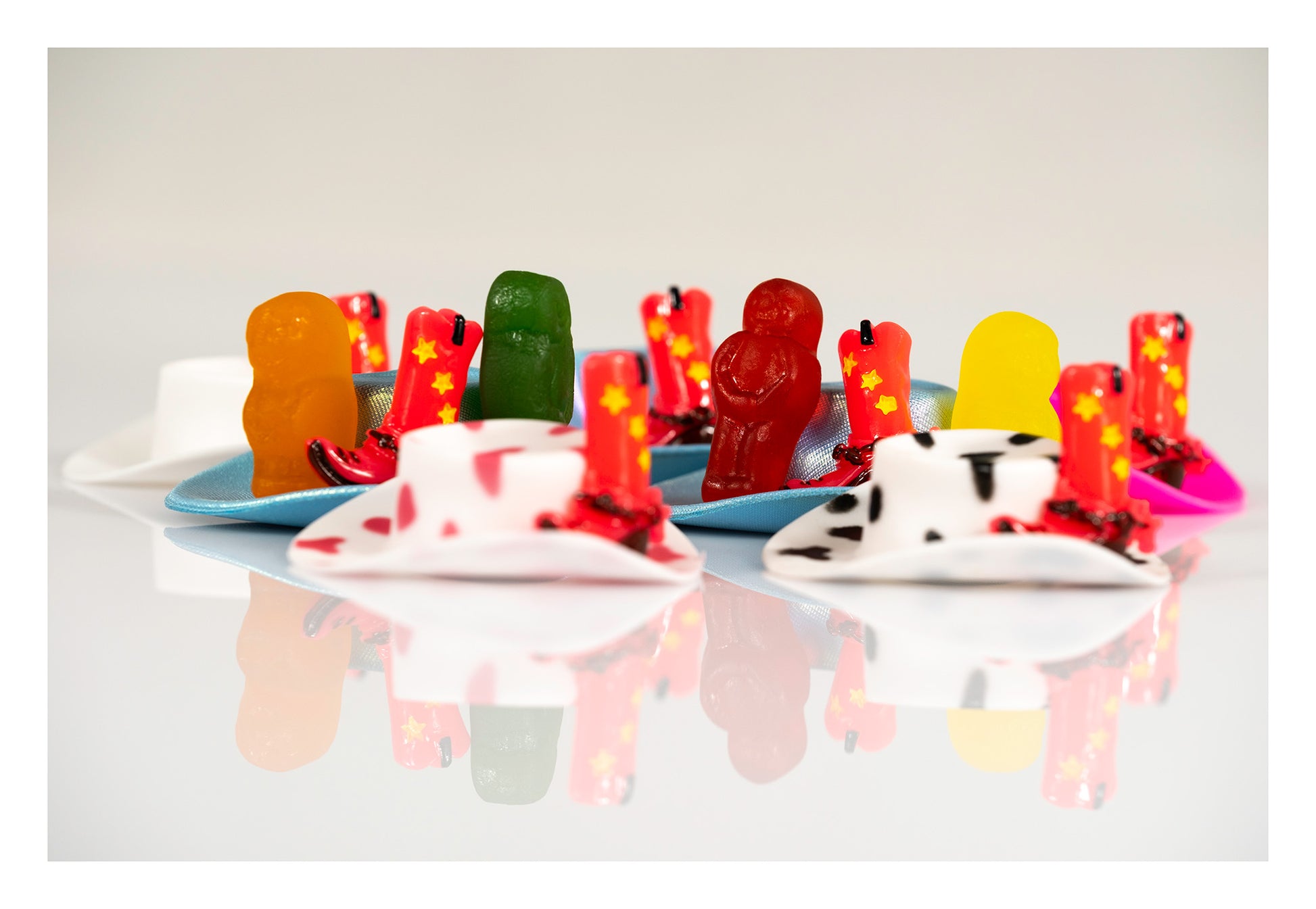 Colourful gummy figures and miniature red cowboy boots arranged on blue hats in a contemporary still life.