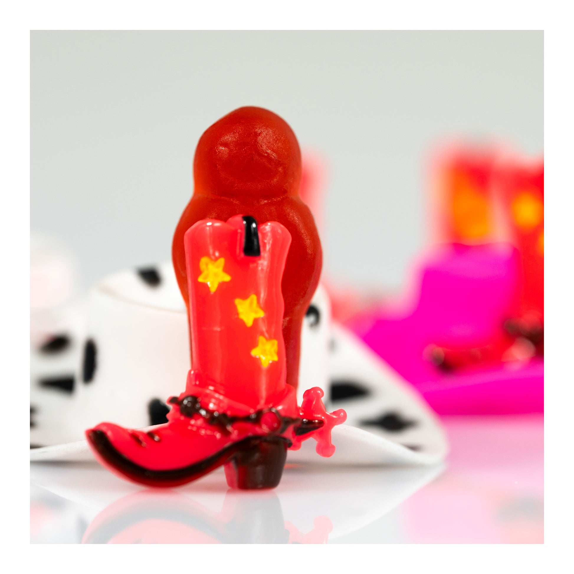 Boot Scootin’ Baby 266831v1 showing a miniature red cowboy boot with yellow stars in front of a red jelly baby, presented with a white print border.