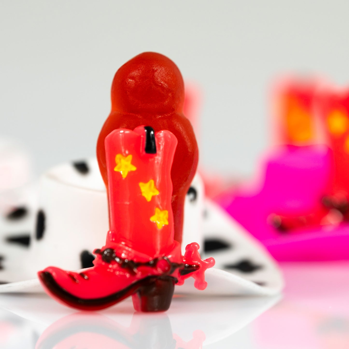 Boot Scootin’ Baby 266831v1, a colourful still life photograph of a miniature red cowboy boot positioned in front of a red jelly baby on a bright white setting.