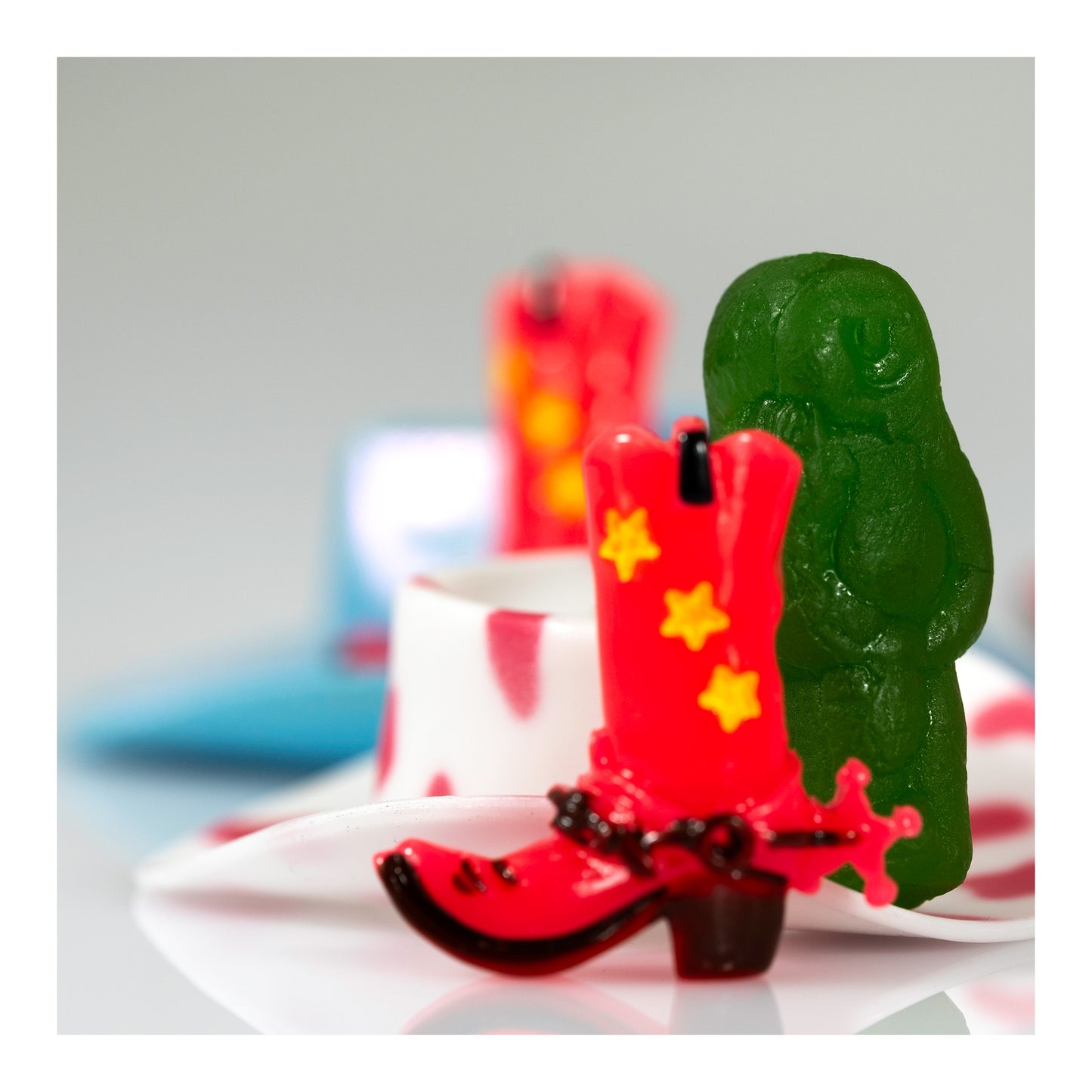 Boot Scootin’ Baby 266835v1 showing a miniature red cowboy boot with yellow stars in front of a green jelly baby, presented with a white print border.