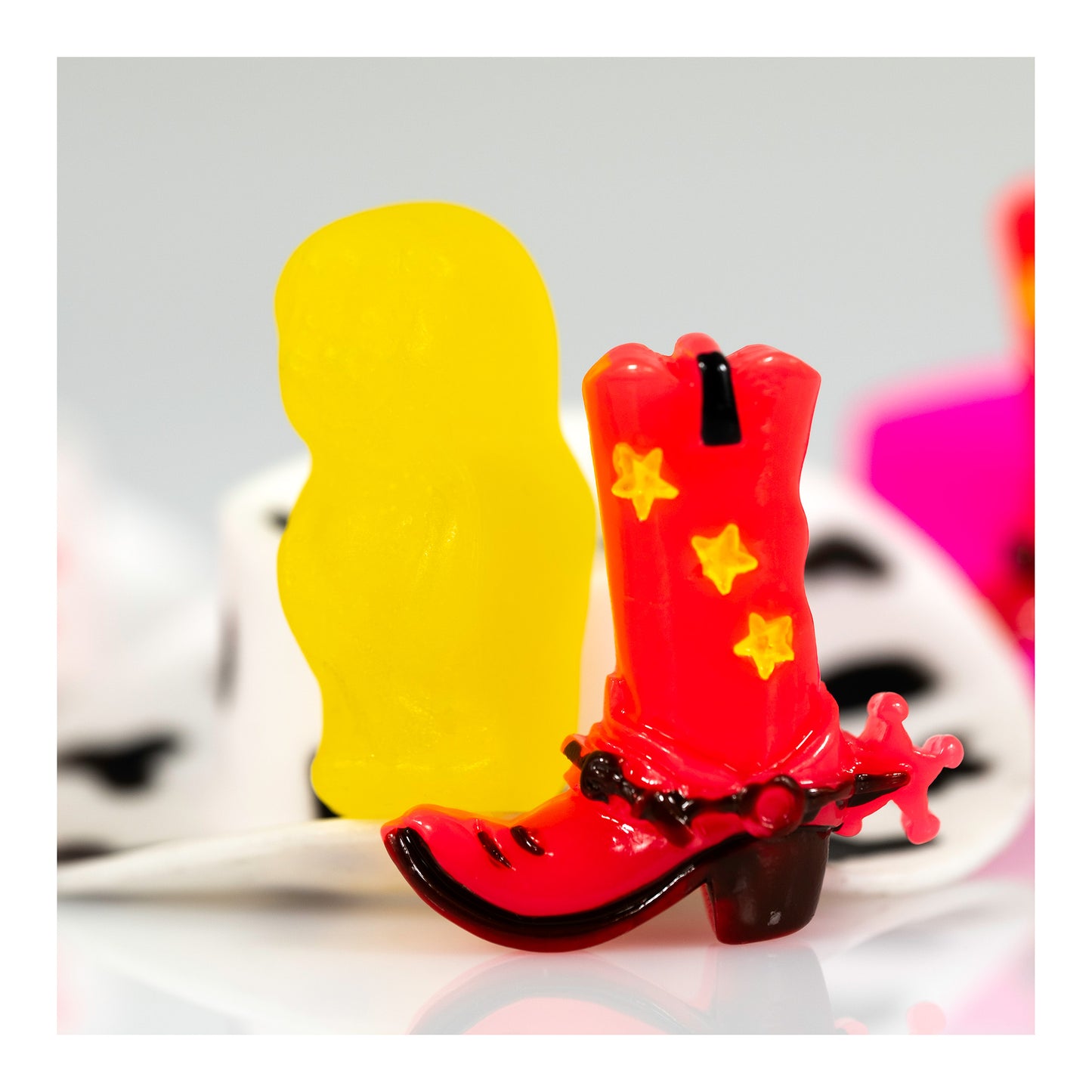 Boot Scootin’ Baby 266838v1 showing a miniature red cowboy boot with yellow stars beside a bright yellow figure, with black-and-white and pink forms behind, presented with a white print border.