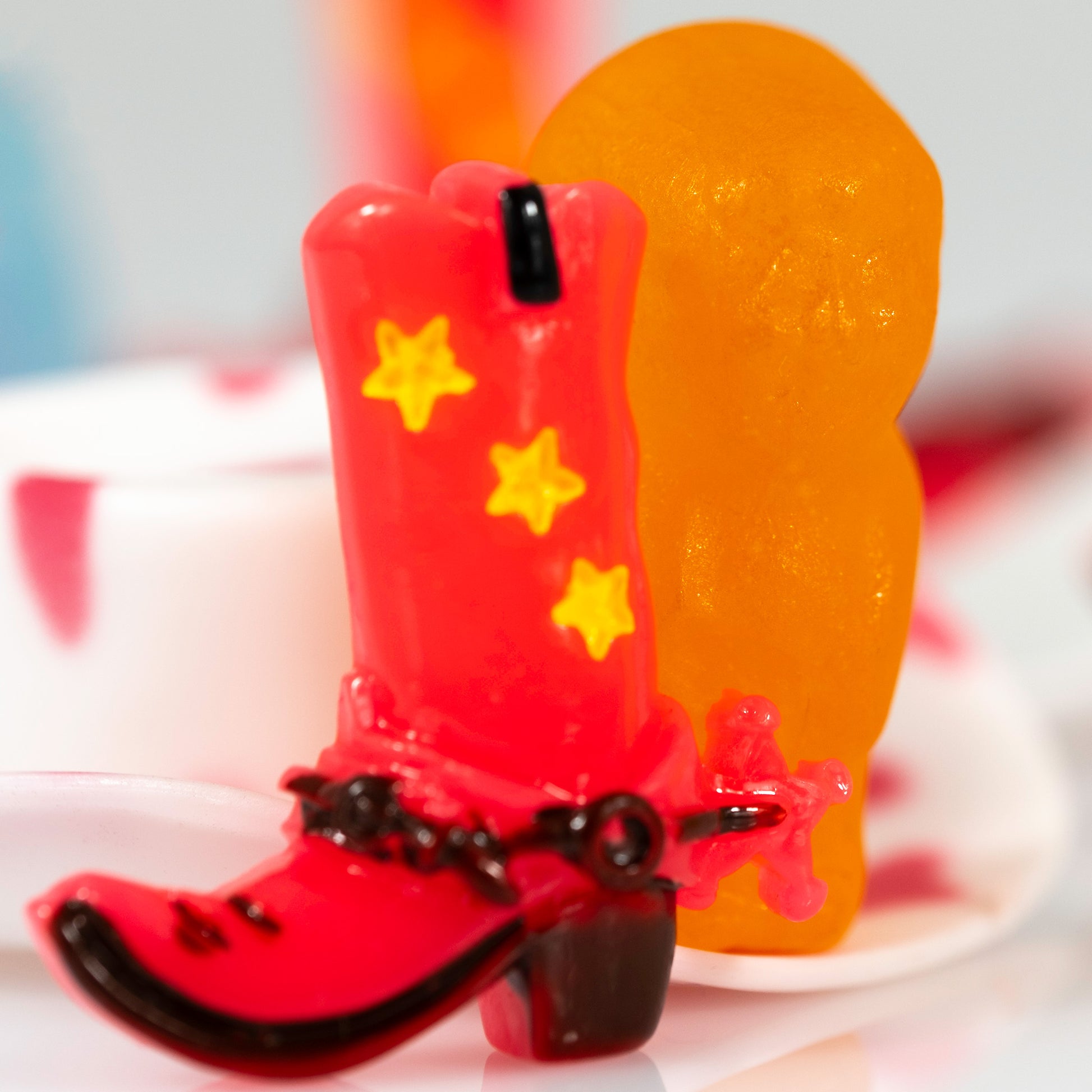 Close crop of a miniature red cowboy boot with yellow stars positioned in front of a translucent orange figure in Boot Scootin’ Baby 266841v1.