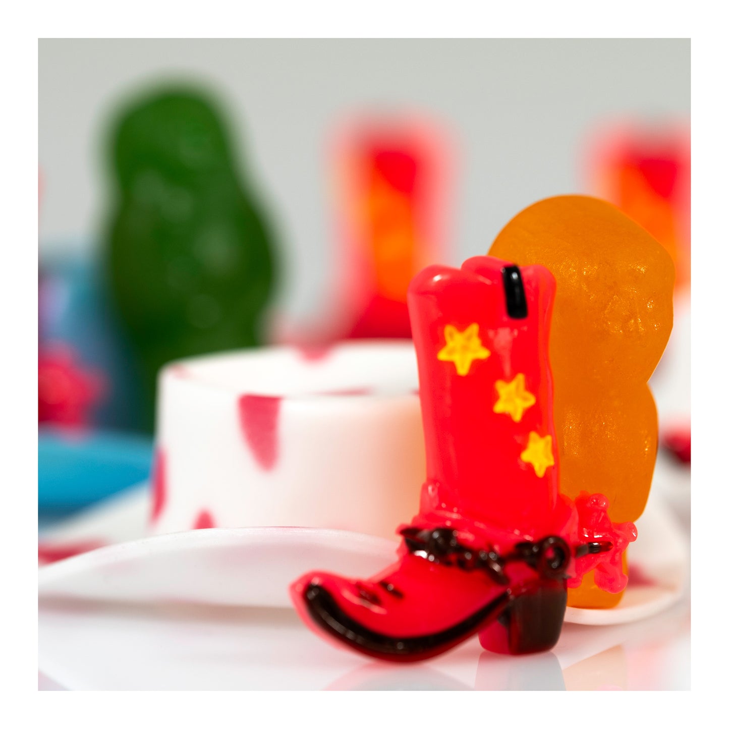Red miniature cowboy boot beside an orange figure with softly focused green and repeated red forms in the background.