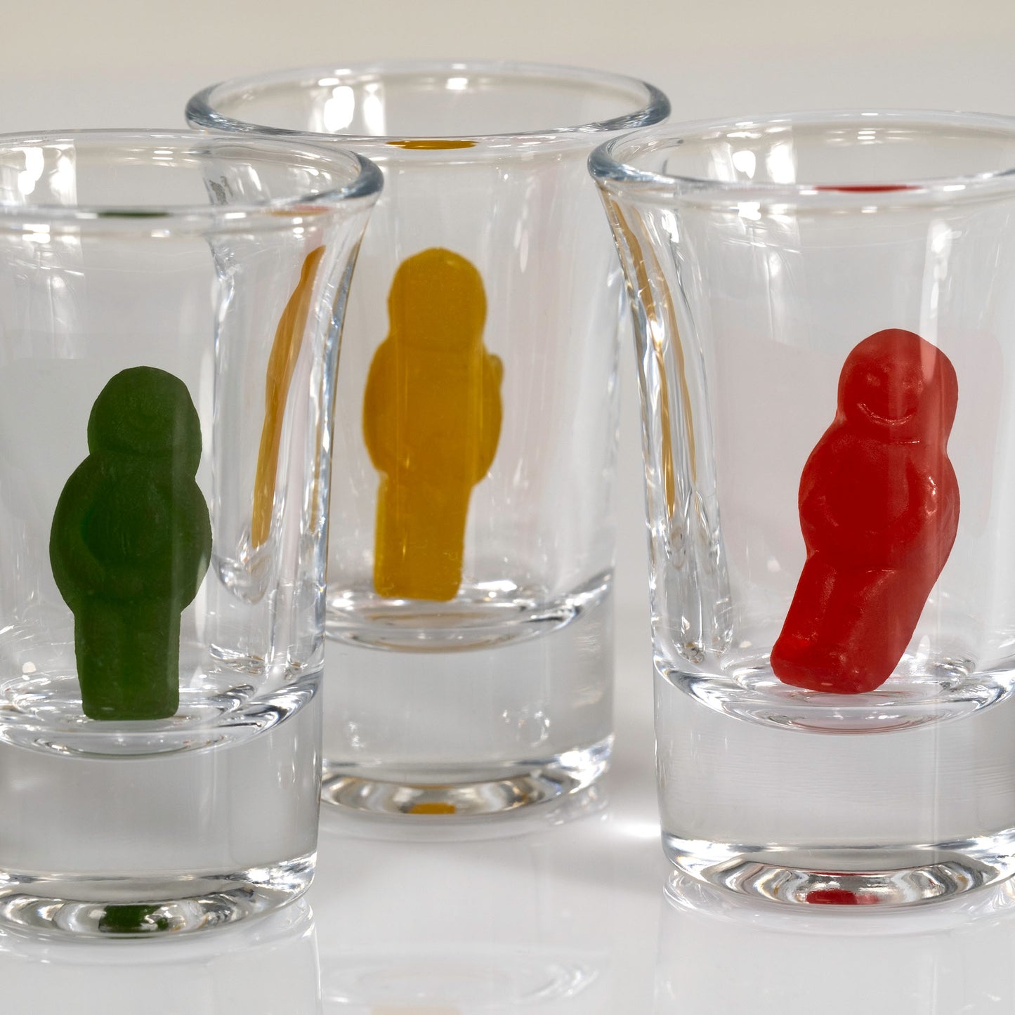 Close-up of green, yellow and red miniature figures standing inside three overlapping clear shot glasses.