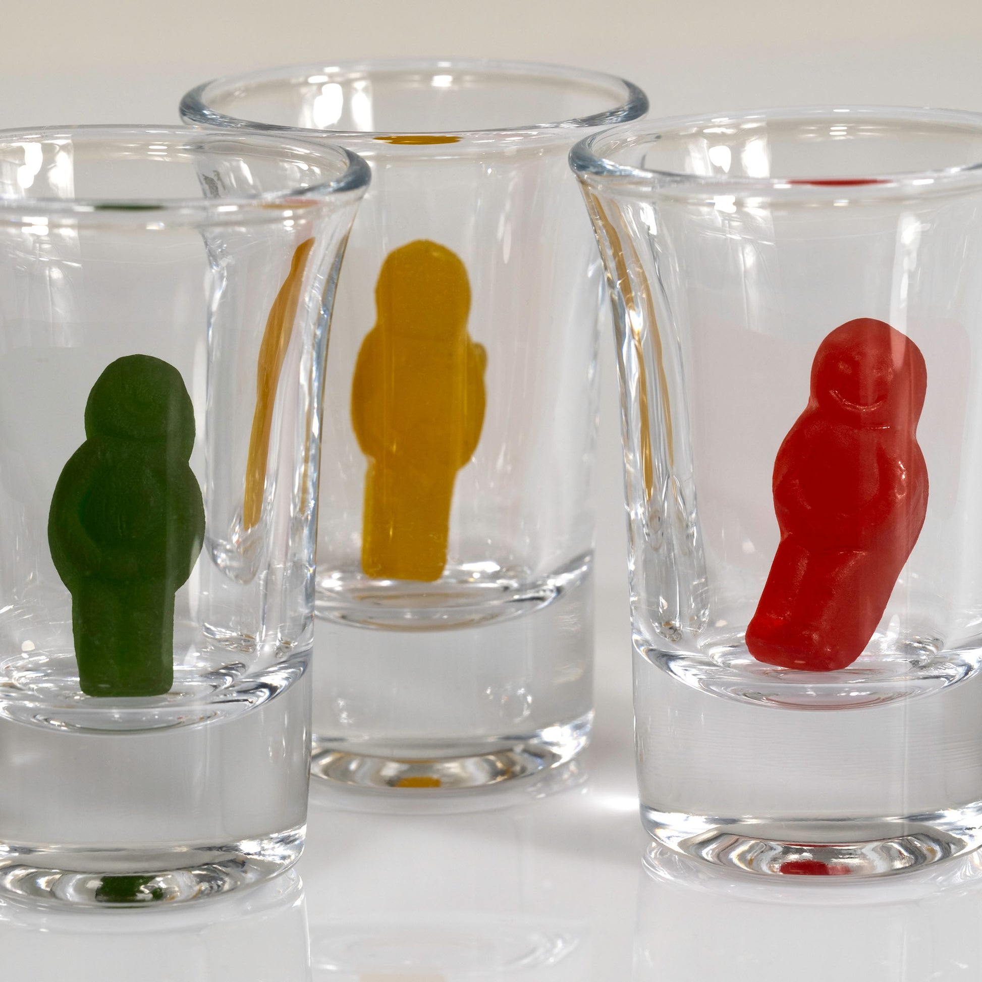 Close-up of green, yellow and red miniature figures standing inside three overlapping clear shot glasses.